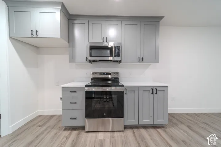 Kitchen featuring grey shaker-style cabinetry, white solid-surface countertops, wood-finish flooring, and stainless steel appliances including an over-the-range microwave and electric range