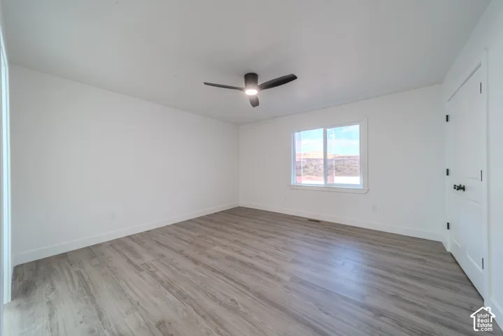 Room featuring wood-finish flooring, a multi-pane window, and a matte black ceiling fan