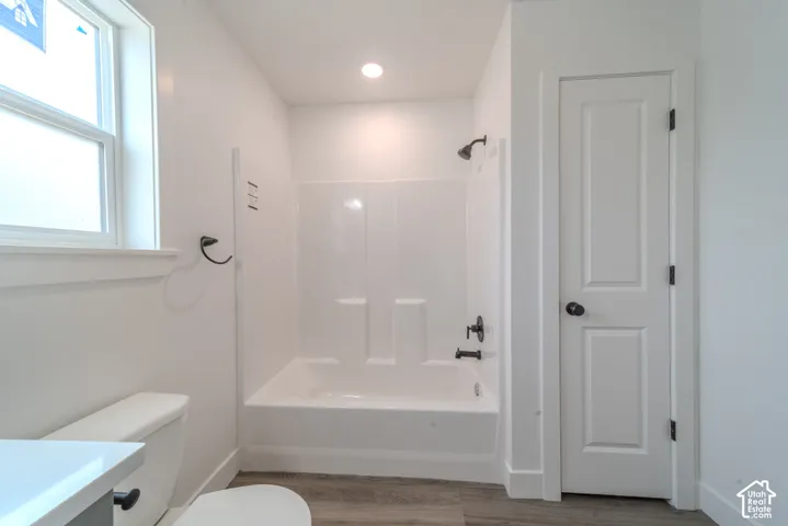 Bathroom featuring a white integrated tub and shower surround, matte black plumbing fixtures, wood-finish flooring, and a solid-core door with matte black hardware