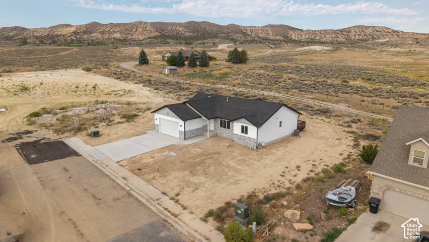 Single-level residence featuring a multi-gabled asphalt shingle roof, stone veneer accents, concrete driveway, and attached two-car garage, set against a desert mountain backdrop
