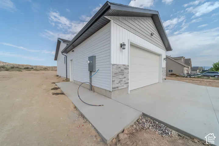 Exterior featuring a two-car garage, mix of white horizontal siding and vertical board-and-batten siding, stone veneer accents, and a concrete driveway