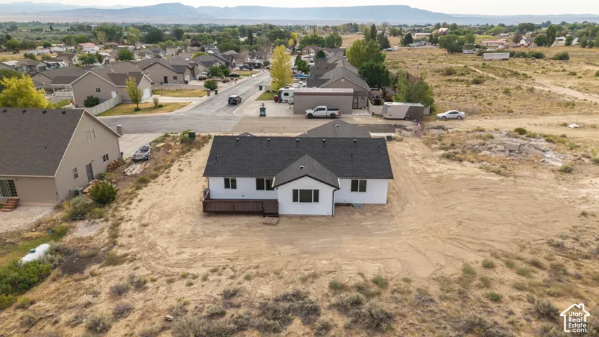 Single-story residence featuring a dark shingled roof, white exterior siding, and an attached rear deck, situated on a large lot with expansive natural desert landscape