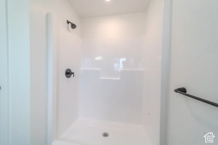 Shower stall featuring a white acrylic surround, matte black shower head, matte black single-handle mixing valve, and a matte black towel bar