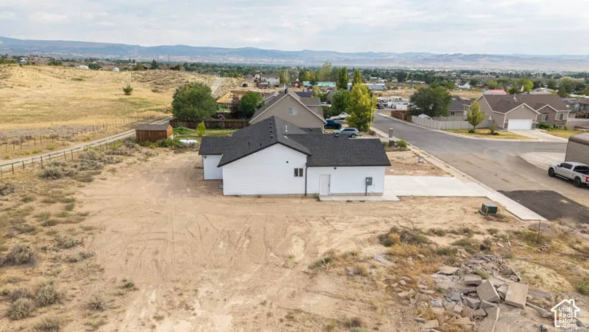Single-story residence featuring a white exterior, dark shingled roof, concrete driveway, and expansive lot with mountain scenery