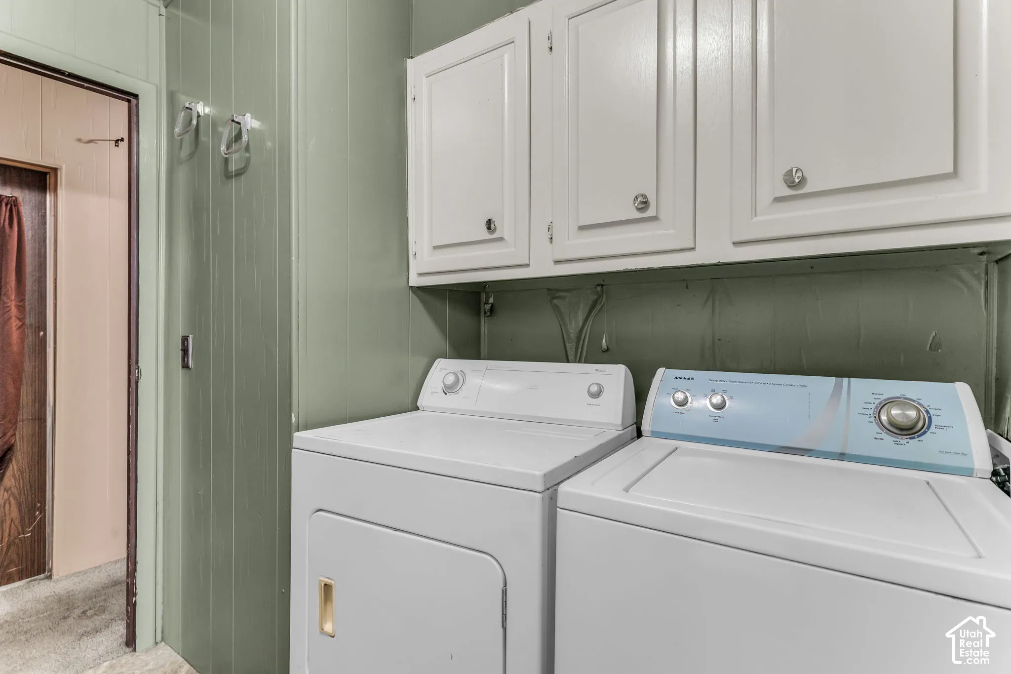 Laundry area featuring white built-in upper cabinetry, vertical paneling, and wall-mounted metal hooks