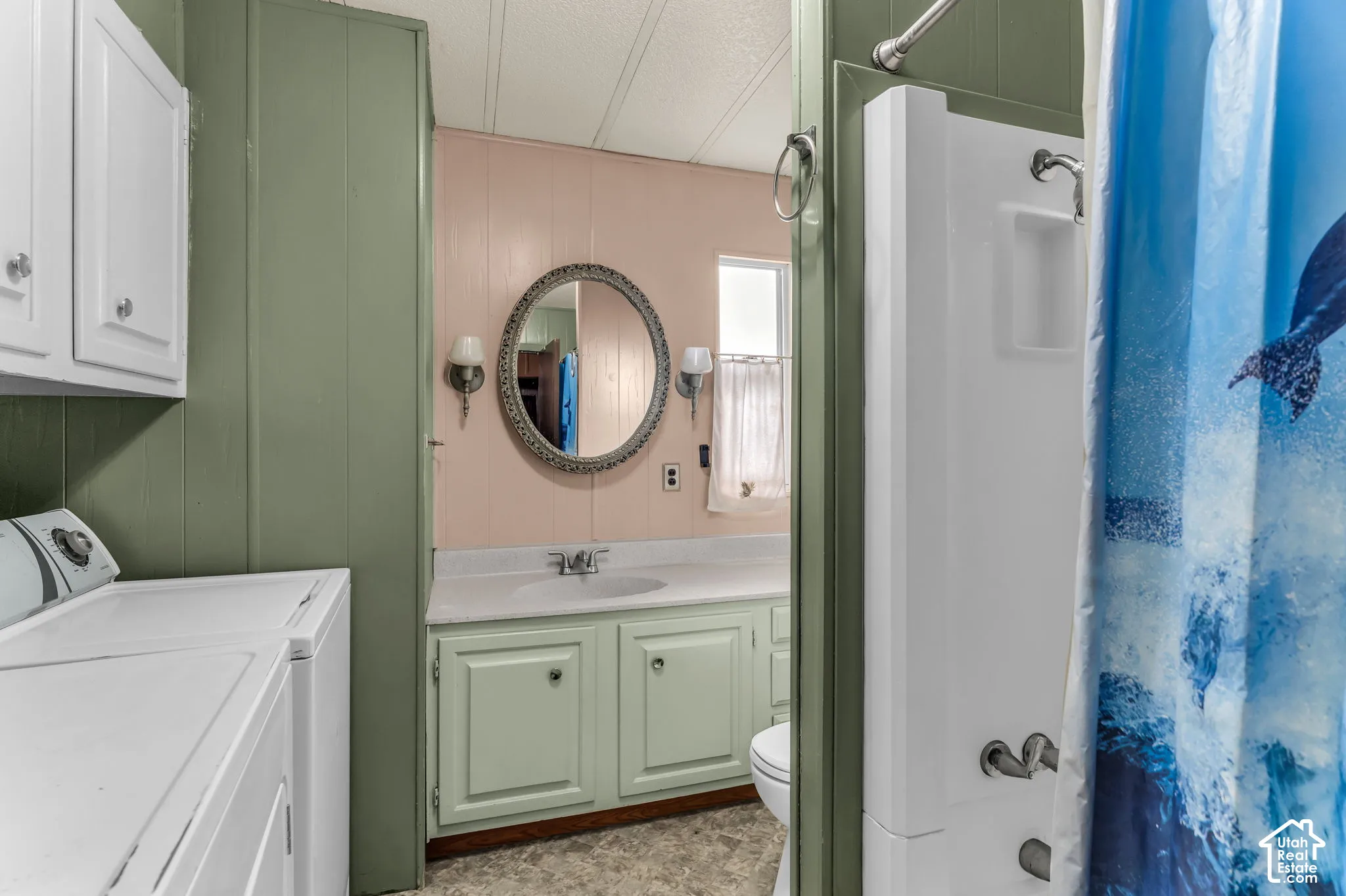 Bathroom featuring a built-in vanity with light-colored cabinetry, a neutral solid-surface countertop, an integrated sink, an oval wall-mounted mirror, and a standalone shower unit