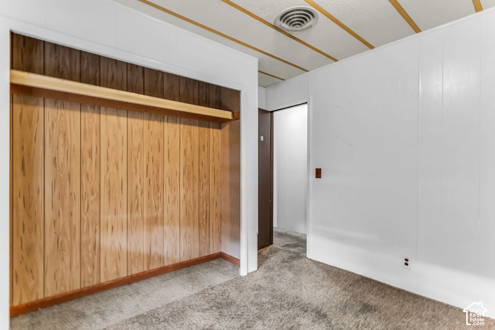 Room featuring wood-paneled wall detail with integrated shelving, textured ceiling, and carpeting
