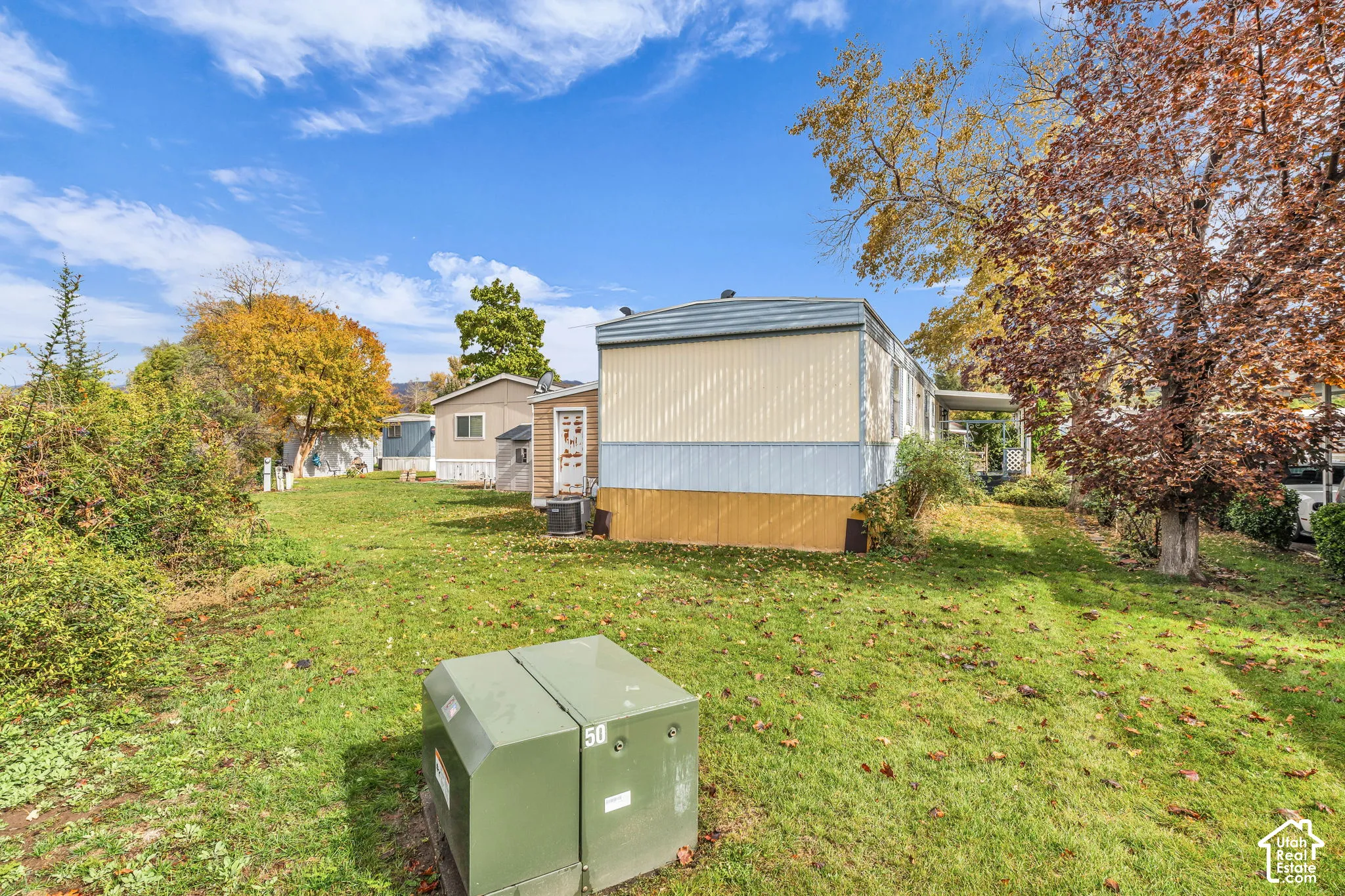 Exterior lot featuring an expansive grass lawn, mature deciduous trees, and metal siding construction