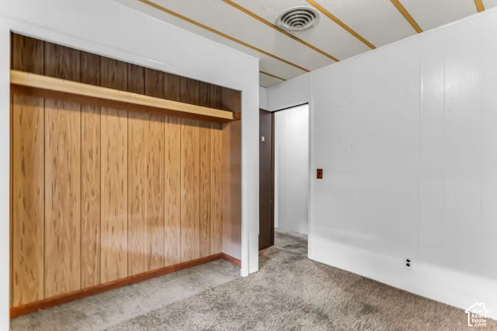 Room featuring wood-paneled wall detail with integrated shelving, textured ceiling, and carpeting