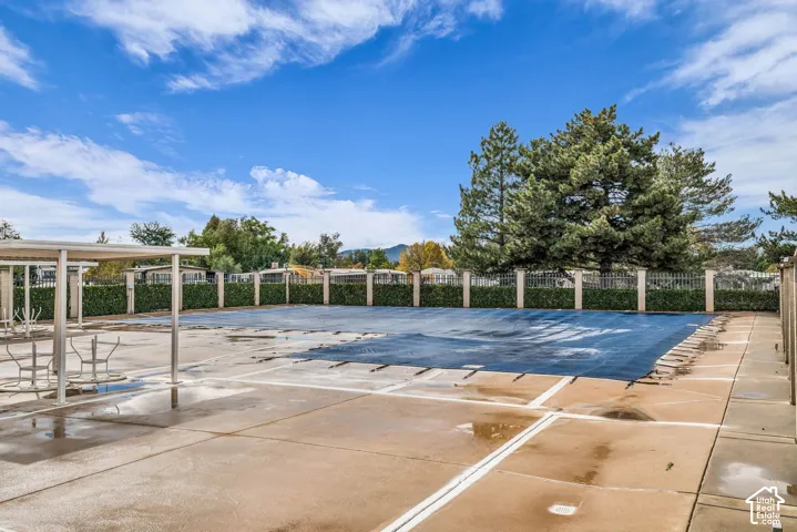 Swimming pool with a secure cover, concrete pool deck, metal-frame shade structure, perimeter fencing, and mature trees