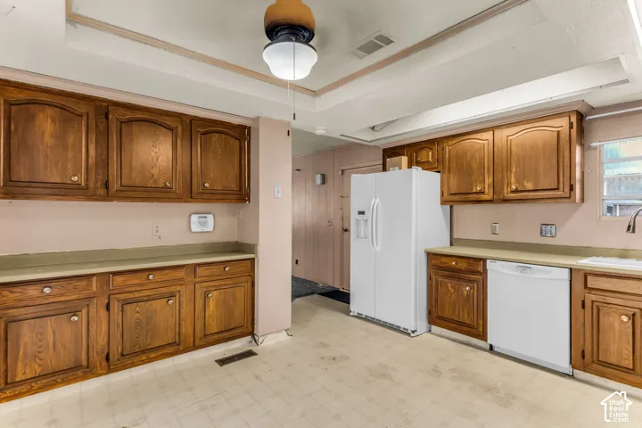 Kitchen featuring wood cabinetry, recessed tray ceiling, white side-by-side refrigerator, white dishwasher, and integrated lighting
