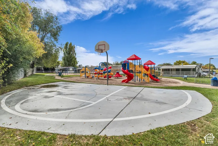 Outdoor recreation area featuring a concrete basketball court, integrated hoop, and a multi-component playground structure