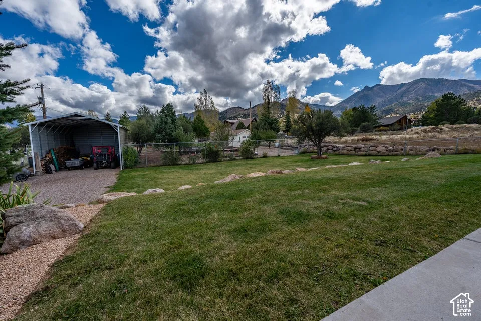 Expansive lawn with rock landscaping, metal-framed carport, and mountain backdrop