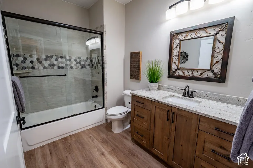 Bathroom featuring a wood-finish vanity with a stone countertop, an integrated rectangular sink, a glass-enclosed shower with decorative hexagon tile inlay, and wood-finish flooring