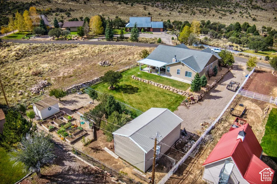 Aerial view of property featuring a single-story residence with a covered patio, a detached garage, a secondary structure with a metal roof, tiered stone retaining walls, and raised garden beds