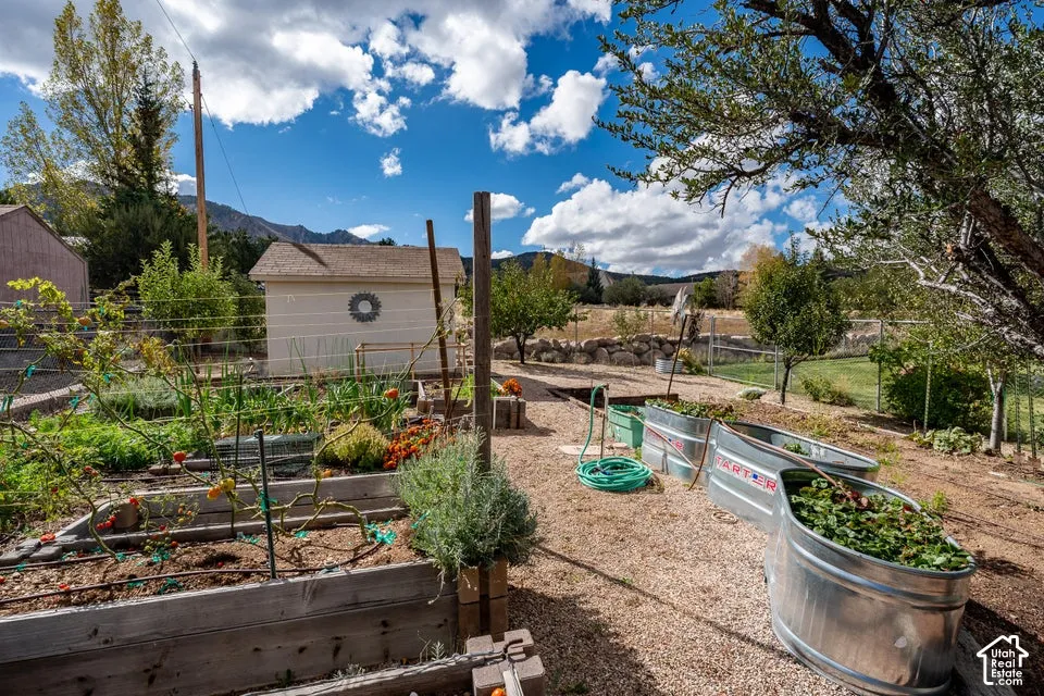 Exterior gardening space featuring wooden raised garden beds, galvanized steel troughs, gravel ground cover, and a detached storage structure