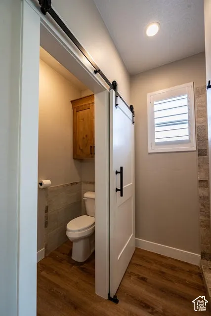 Sliding barn door with matte black hardware, wood-finish flooring, wall-mounted natural wood cabinetry, recessed ceiling lighting, and window shutter