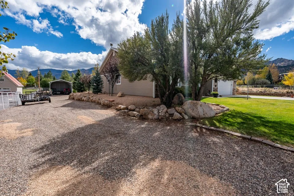 Exterior featuring gravel driveway, rock landscaping, mature trees, lawn, and mountain backdrop