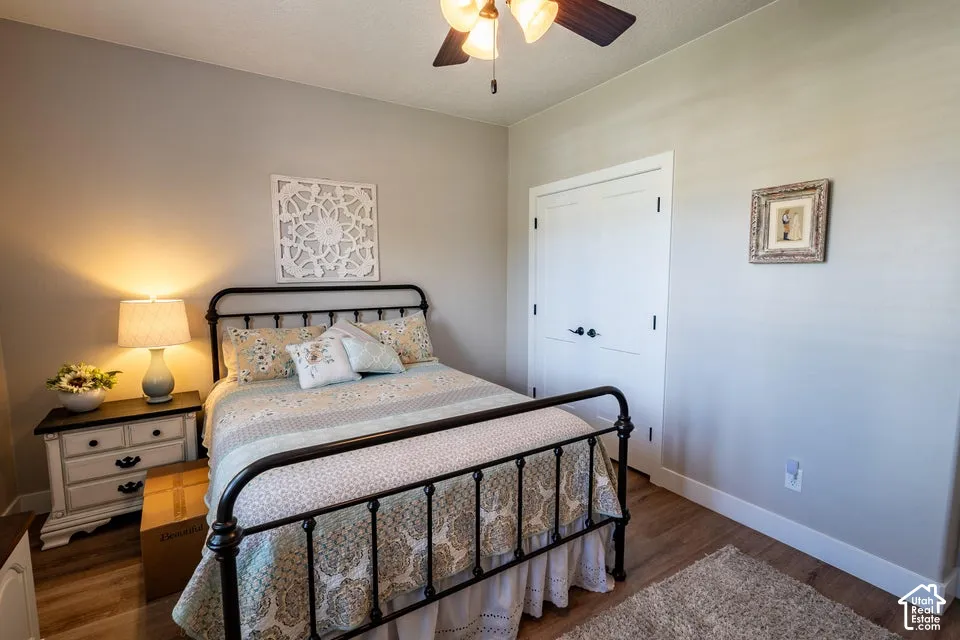 Neutral-toned room featuring wood-finish flooring, a ceiling fan with integrated lighting, and white double-door closet with matte black hardware