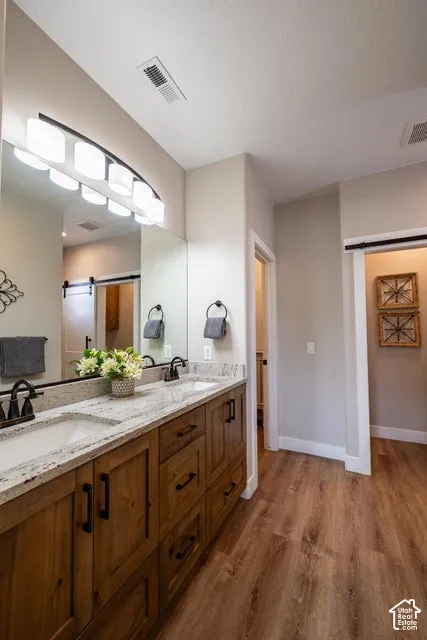 Bathroom featuring a dual-sink vanity with stone countertops, wood-finish cabinetry, dark metallic fixtures, and a sliding barn-style door