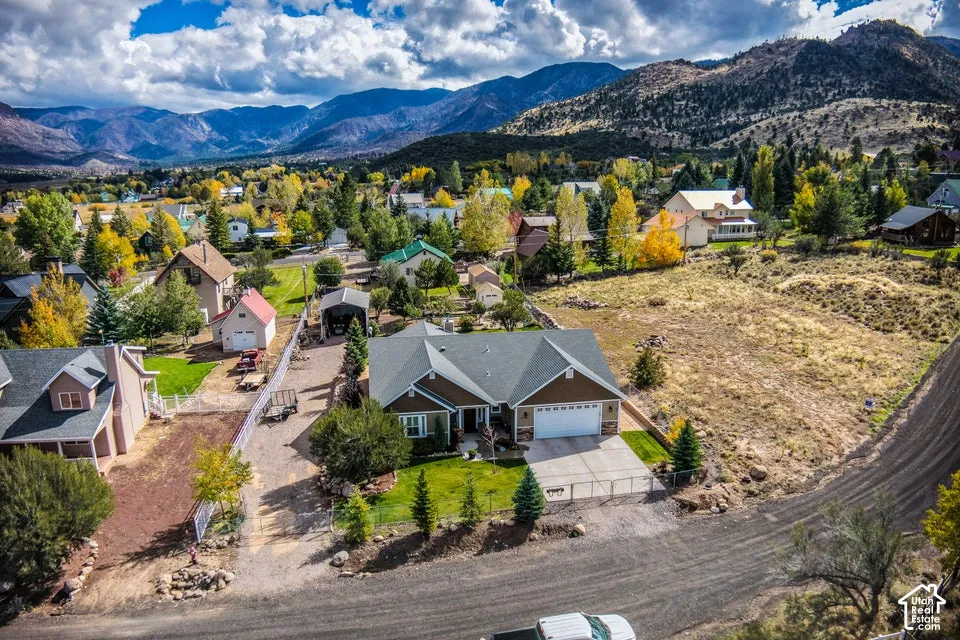 Single-level residence featuring a multi-gabled roof, attached two-car garage, concrete driveway, and fenced perimeter, situated against a mountain backdrop