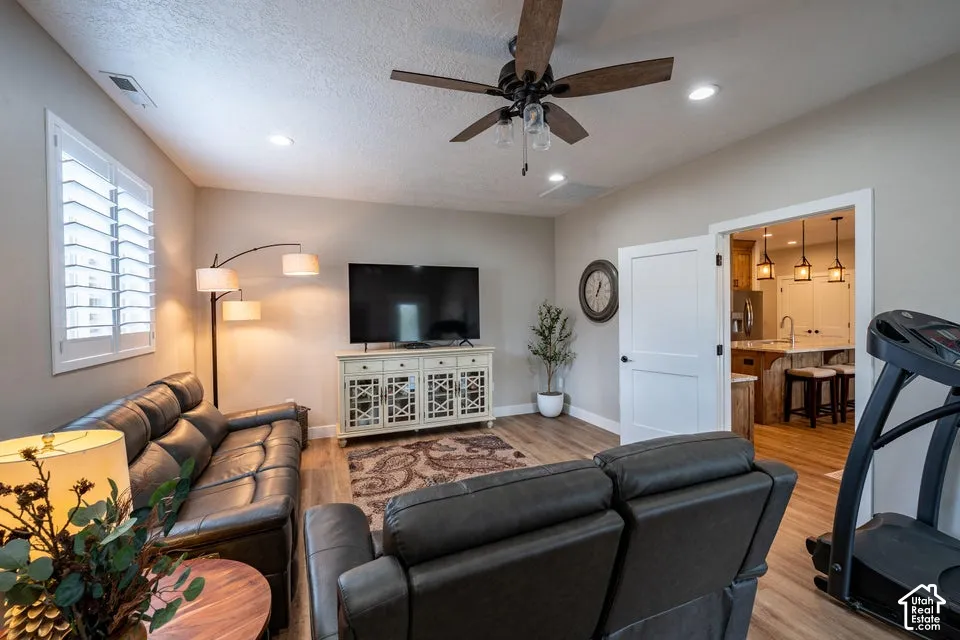 Living area featuring wood-finish flooring, recessed lighting, ceiling fan with light fixture, and plantation shutters