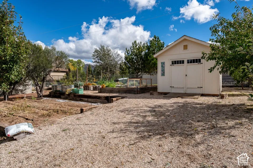 Exterior grounds featuring a detached storage shed, raised garden beds, timber retaining walls, gravel landscaping, and mature trees