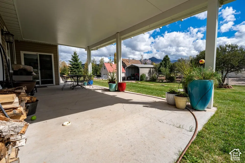 Covered concrete patio featuring structural support pillars, sliding glass door access, and mountainous scenery