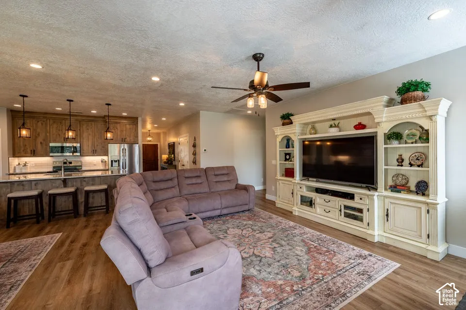 Open-concept interior featuring wood-finish flooring, custom built-in cabinetry, recessed lighting, a ceiling fan, and stained wood kitchen cabinetry
