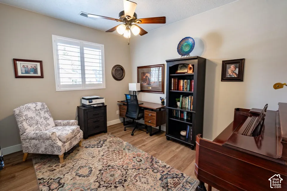 Wood-finish flooring, plantation shutters, and a central ceiling fan with multi-light fixture