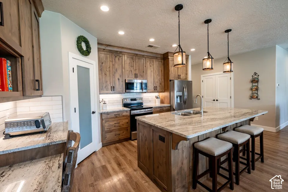 Kitchen featuring natural wood-finish cabinetry, stone-surface countertops, subway tile backsplash, stainless steel appliances, and a central island with pendant lighting