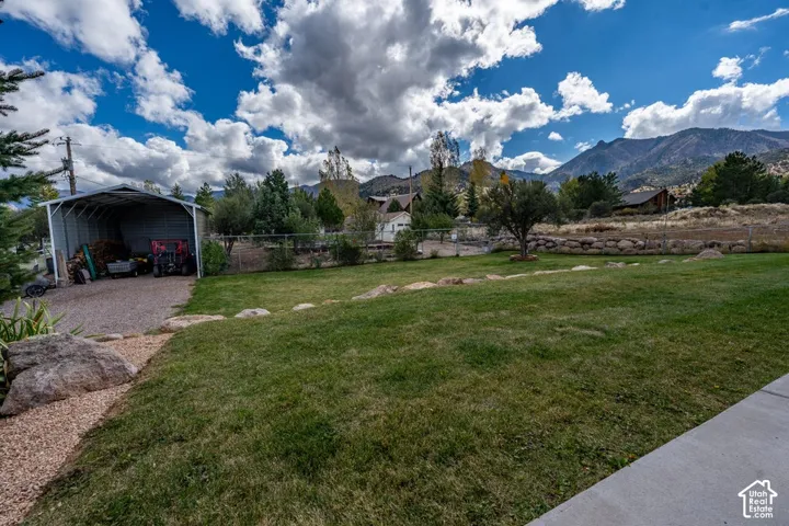 Expansive lawn with rock landscaping, metal-framed carport, and mountain backdrop