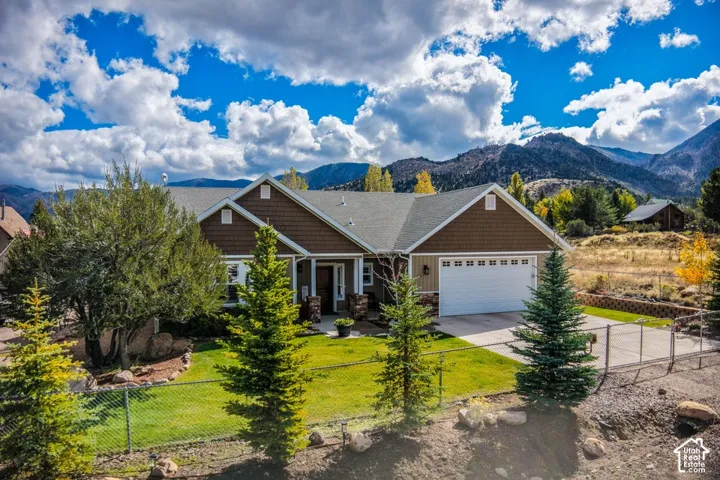 Exterior featuring shingle and horizontal siding, a multi-gabled roofline, stone masonry accents, a paved driveway, and an attached garage set against a mountain backdrop