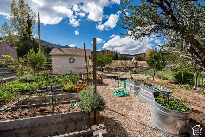 Exterior gardening space featuring wooden raised garden beds, galvanized steel troughs, gravel ground cover, and a detached storage structure