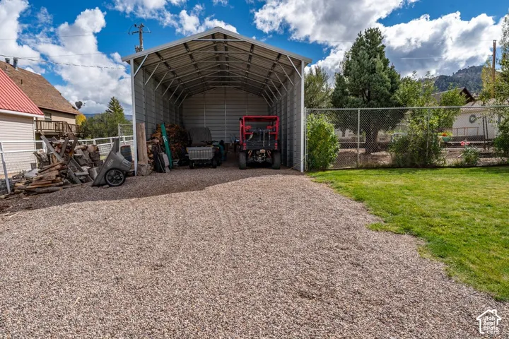 Open-air metal carport featuring a gabled roof, gravel driveway, and chain-link perimeter fencing