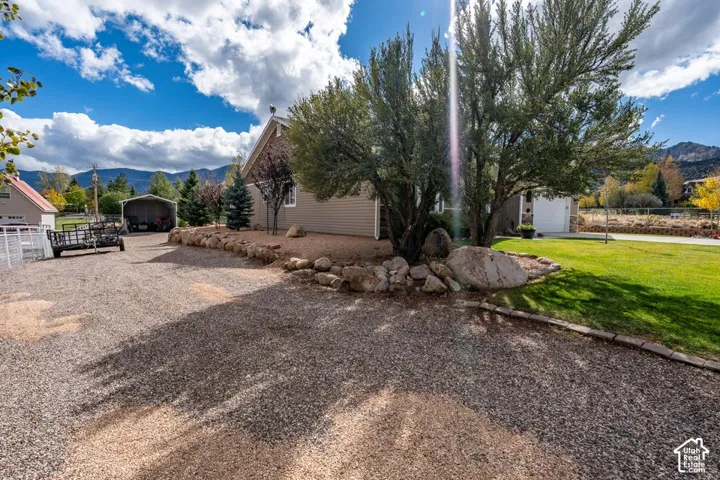 Exterior featuring gravel driveway, rock landscaping, mature trees, lawn, and mountain backdrop