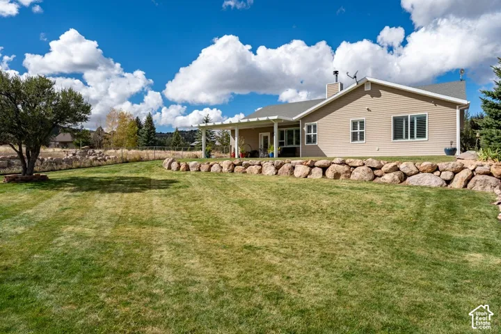Expansive backyard featuring a tiered natural stone retaining wall, covered patio, manicured lawn, and mature landscaping