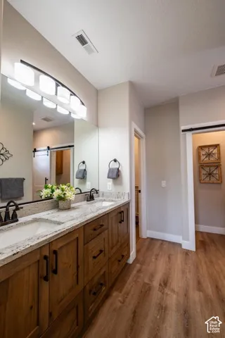 Bathroom featuring a dual-sink vanity with stone countertops, wood-finish cabinetry, dark metallic fixtures, and a sliding barn-style door