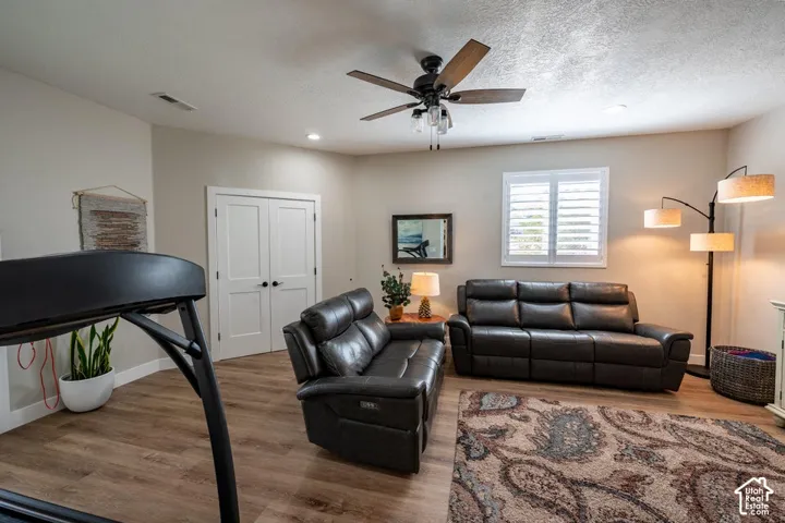 Neutral interior space featuring wood-finish flooring, recessed lighting, a ceiling fan with integrated light fixtures, and window shutters