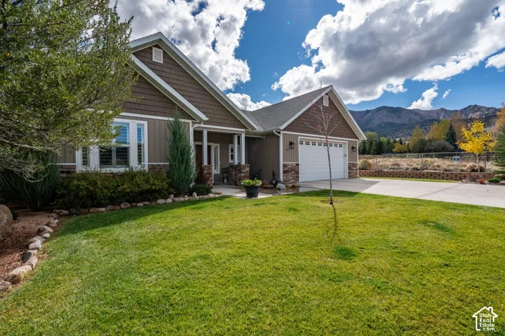 Multi-textured exterior featuring shake and vertical siding, stone veneer accents, an attached two-car garage, and a mountain backdrop