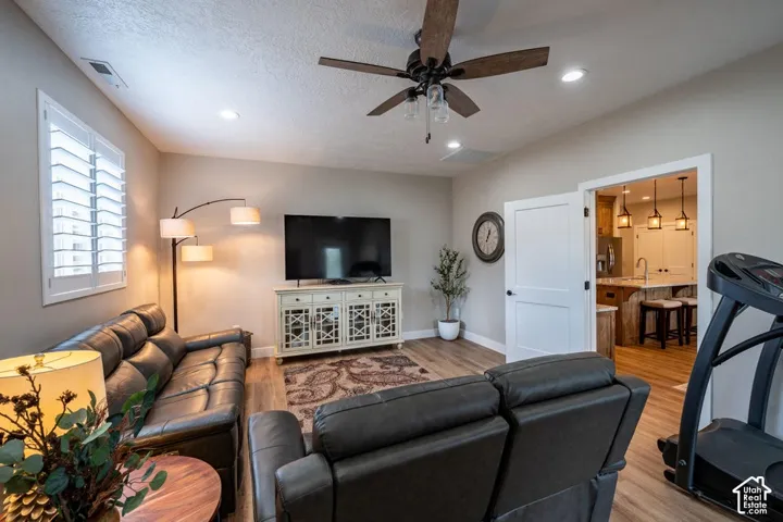 Living area featuring wood-finish flooring, recessed lighting, ceiling fan with light fixture, and plantation shutters