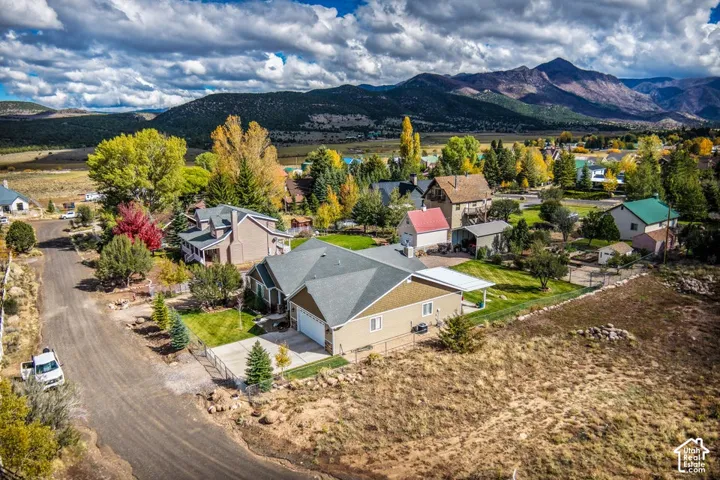 Aerial perspective featuring a single-story residence with an attached two-car garage, concrete driveway, and covered patio, set against a backdrop of mountain ranges