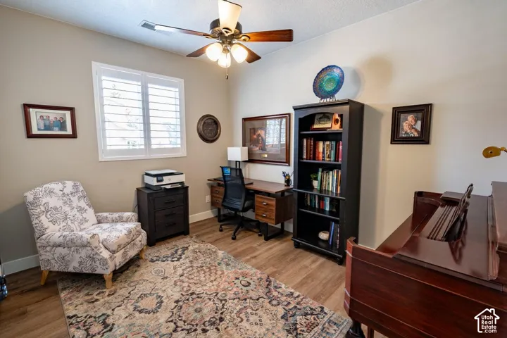 Wood-finish flooring, plantation shutters, and a central ceiling fan with multi-light fixture