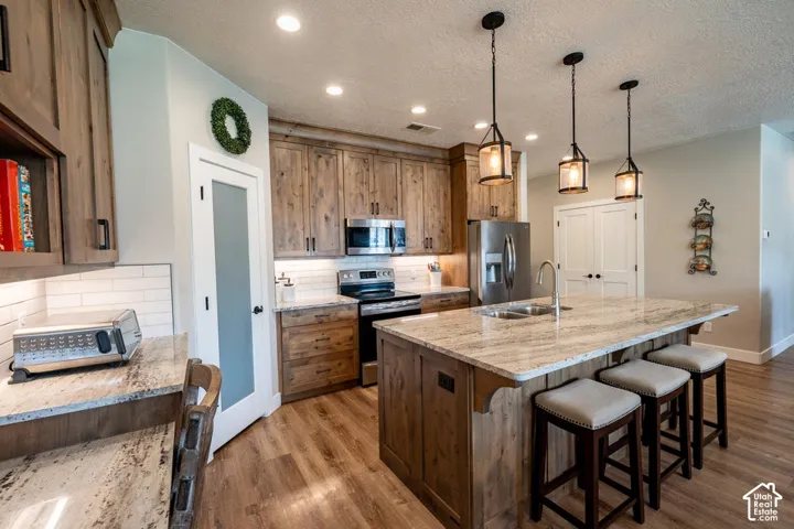 Kitchen featuring natural wood-finish cabinetry, stone-surface countertops, subway tile backsplash, stainless steel appliances, and a central island with pendant lighting