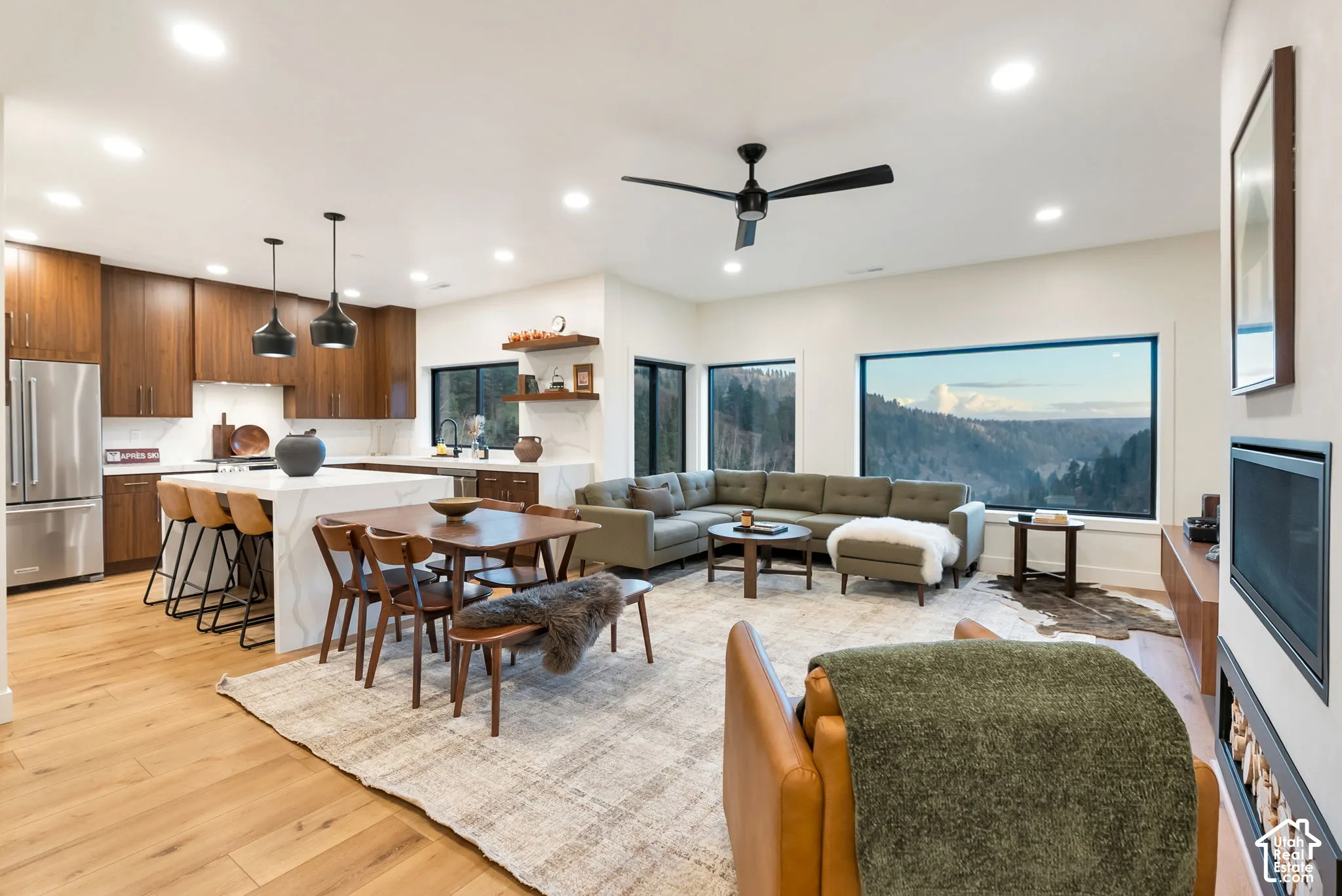 Open-concept interior featuring wood-finish flooring, a kitchen island with quartz countertops, custom cabinetry, a built-in fireplace, and expansive picture windows with mountain scenery