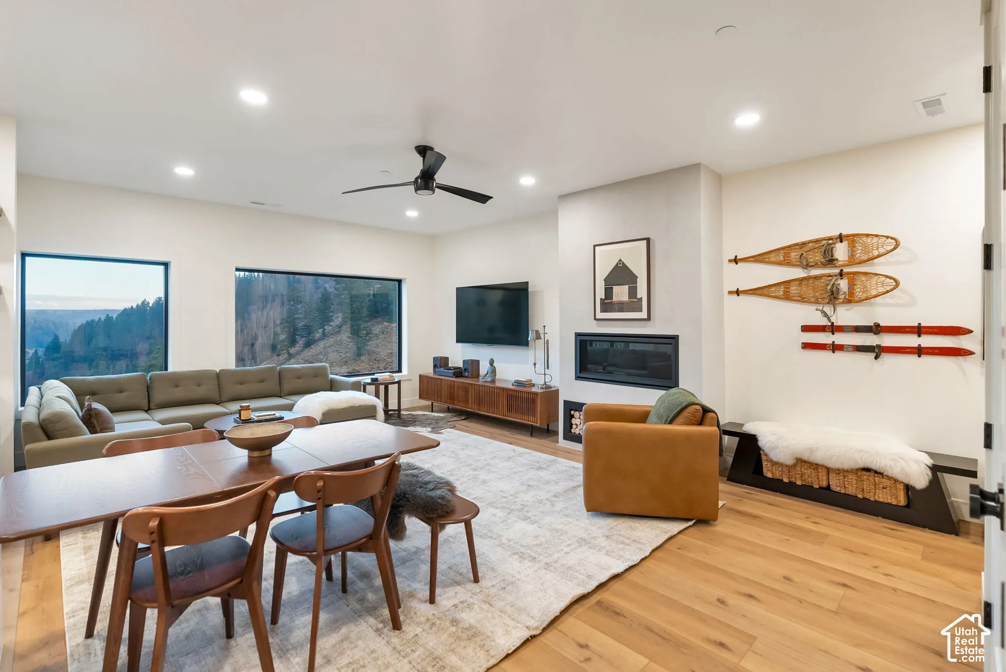 Open-concept living space featuring wood-finish flooring, a linear fireplace with a textured surround, recessed lighting, and large picture windows