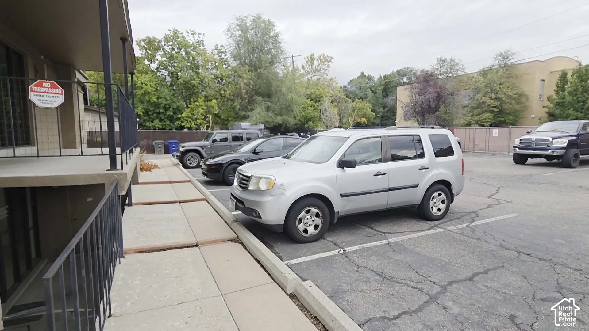 Asphalt-paved parking area with marked stalls, concrete pedestrian walkway, and metal railing