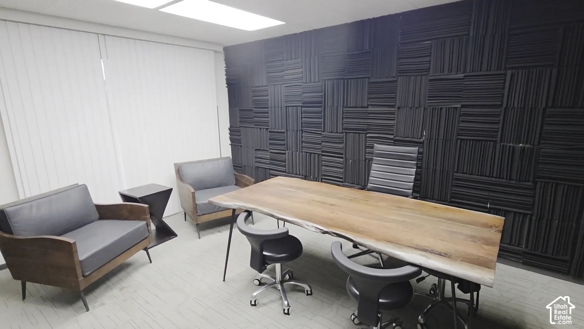Textured black acoustic wall paneling, recessed lighting, and vertical window blinds