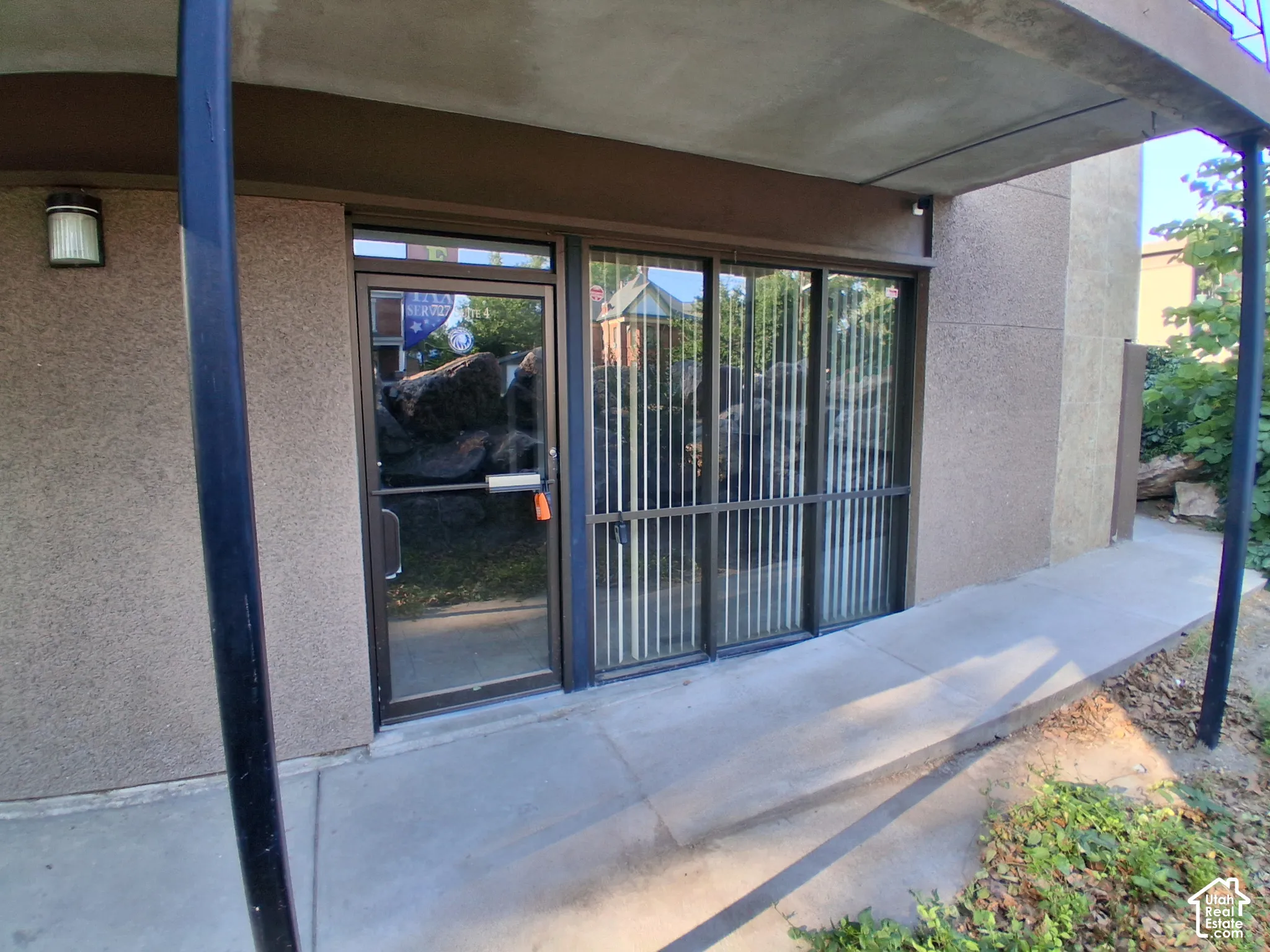 Ground-level entry featuring a concrete porch, metal-framed glass door, expansive floor-to-ceiling windows, and exterior wall-mounted lighting