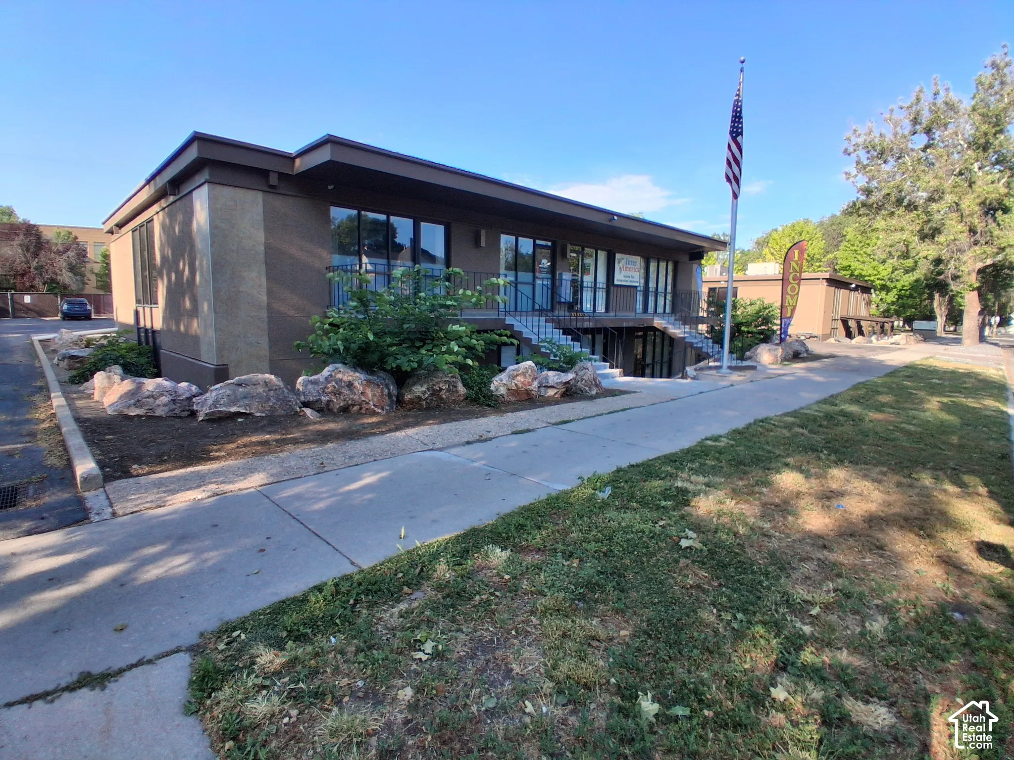 Commercial structure featuring a low-profile flat roof, stucco exterior, large storefront glass windows, and metal staircase entryways complemented by decorative boulder landscaping
